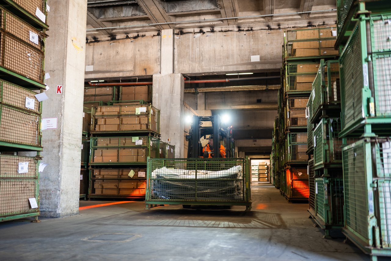 Ein lächelnder Mann in orangefarbener Warnweste fährt einen Gabelstapler in einem Lager.